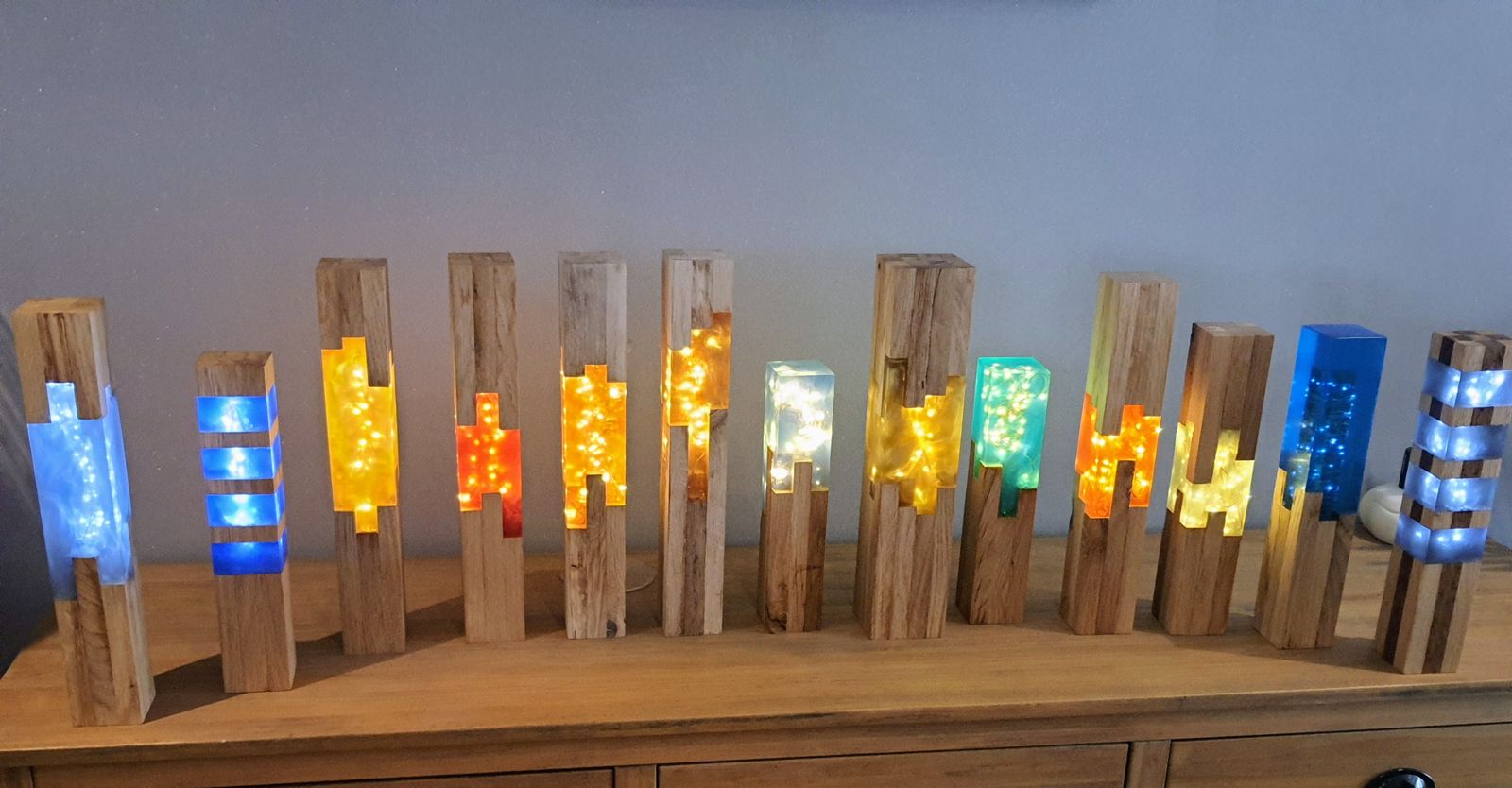 Collection de treize lampes en chêne et résine colorée alignées sur un buffet