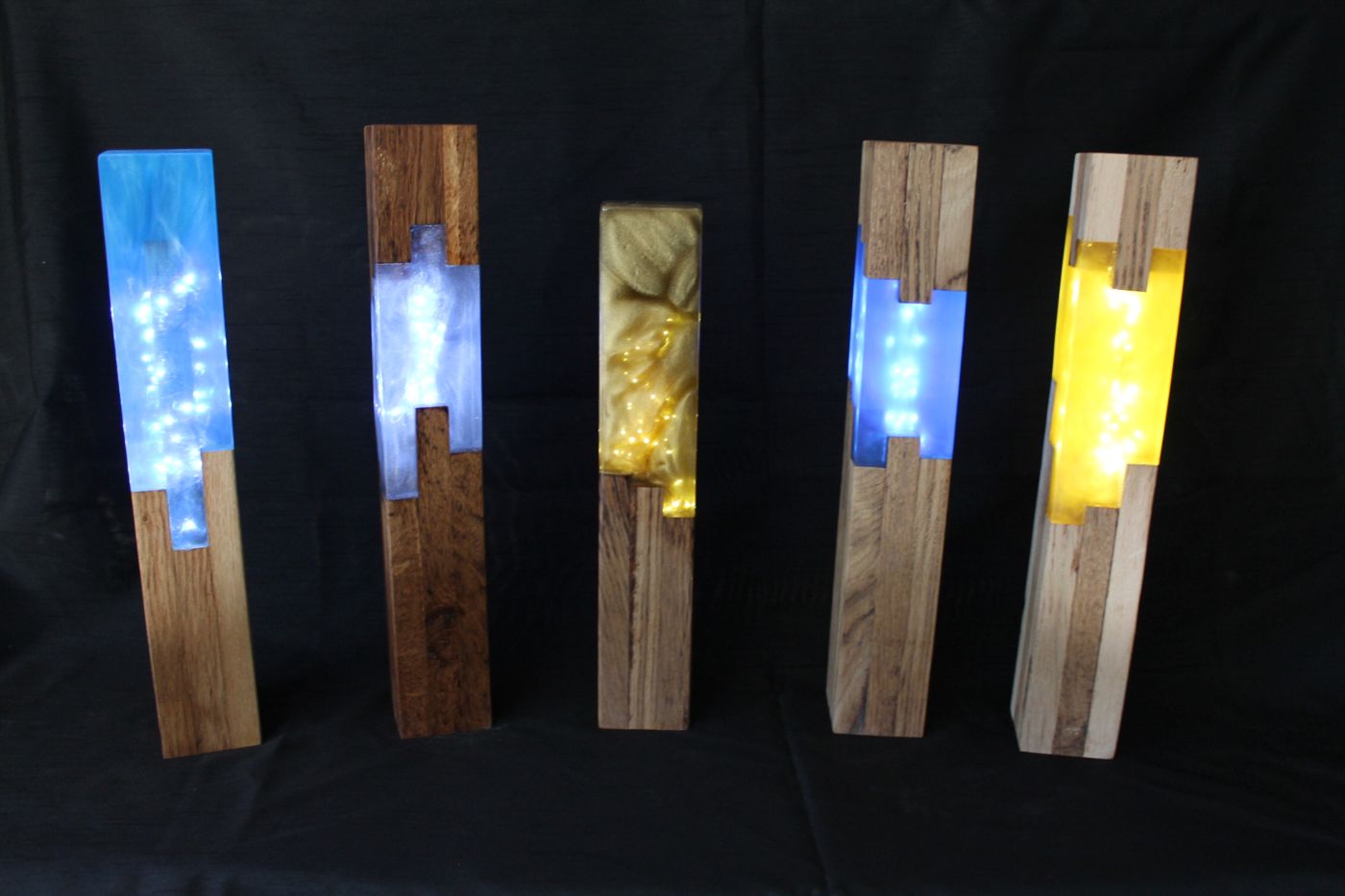 Cinq lampes colonnes en chêne et résine bleue, blanche et dorée, allumées